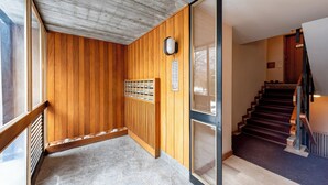 Un intérieur en bois avec un sol en pierre, un banc en bois, un radiateur fixé au mur et un escalier recouvert d’une moquette sombre.