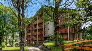 Un immeuble à plusieurs étages doté de balcons, entouré d’arbres et bordé d’un chemin pavé de pierres.