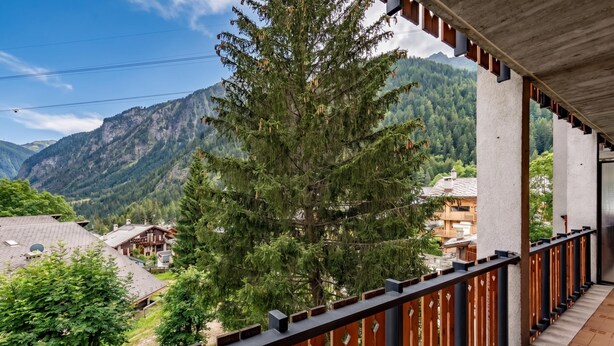 Un balcon donnant sur un paysage montagneux, avec des balustrades en bois et un bâtiment doté d’un toit en pente.