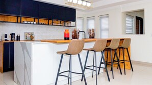 A modern kitchen with a central island, bar stools, and a pendant light.