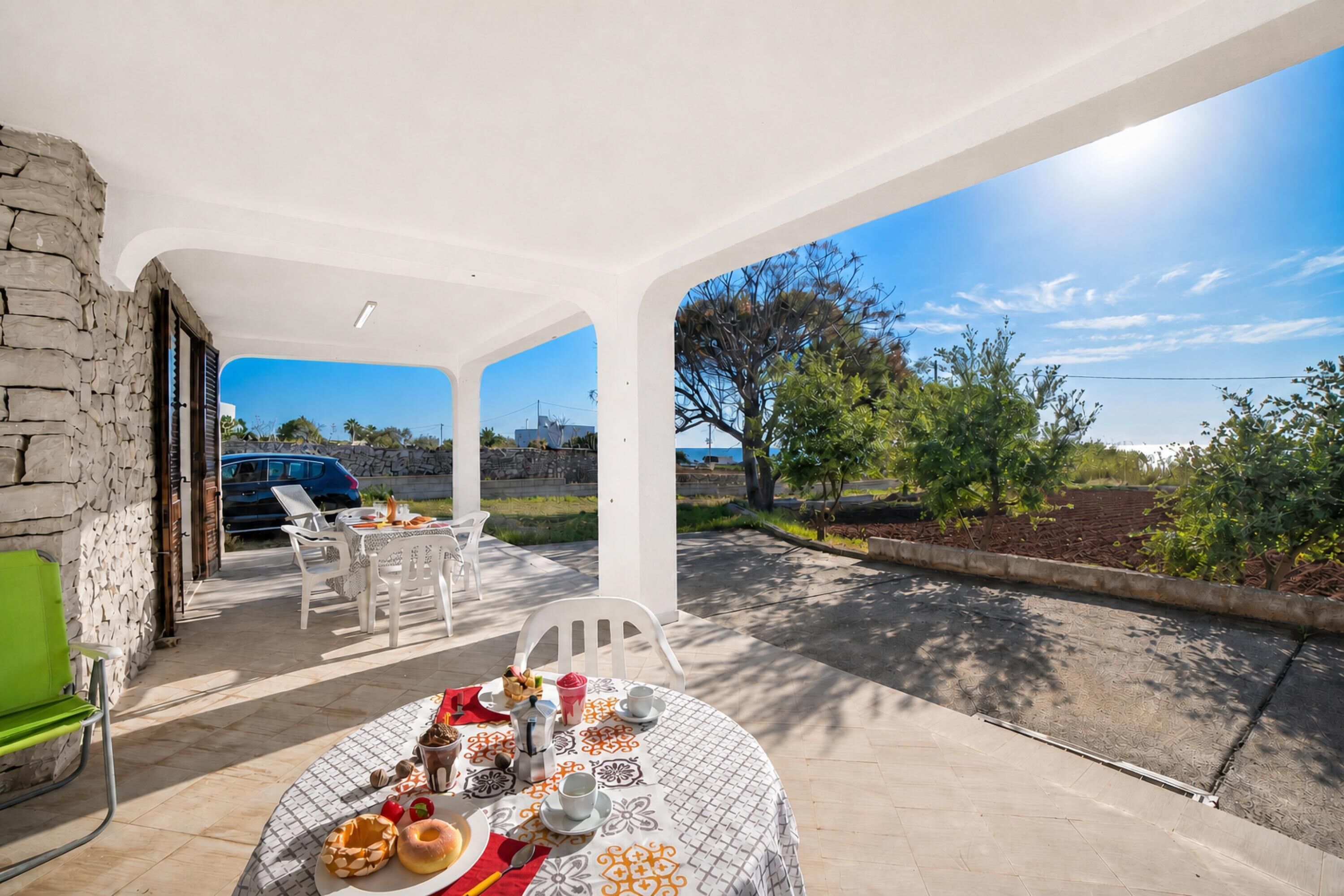 An outdoor dining area with a table set for two, chairs, and a stone wall.