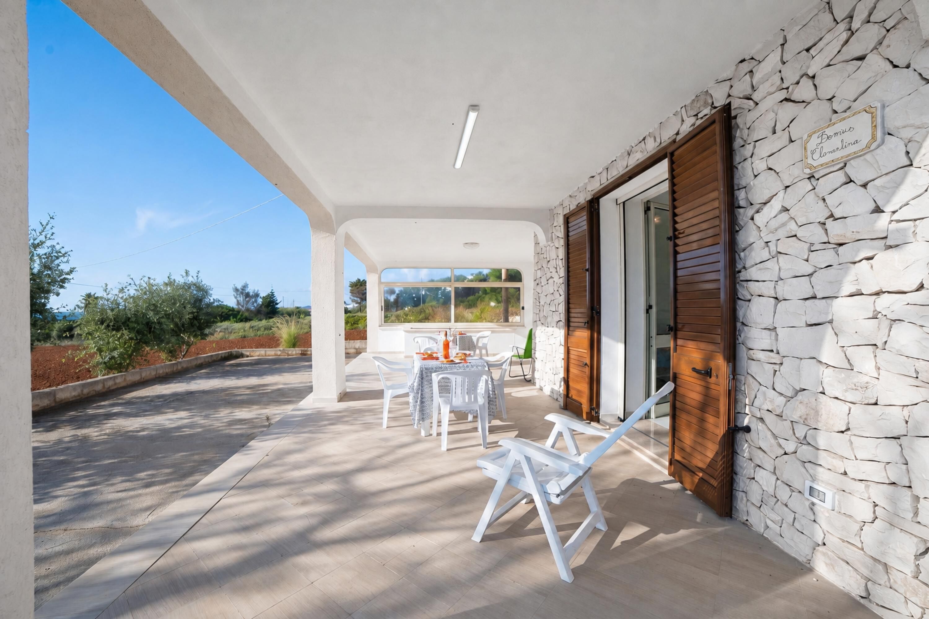 Une terrasse extérieure couverte, dotée d’un mur en pierre, d’une porte en bois et d’une table avec des chaises.
