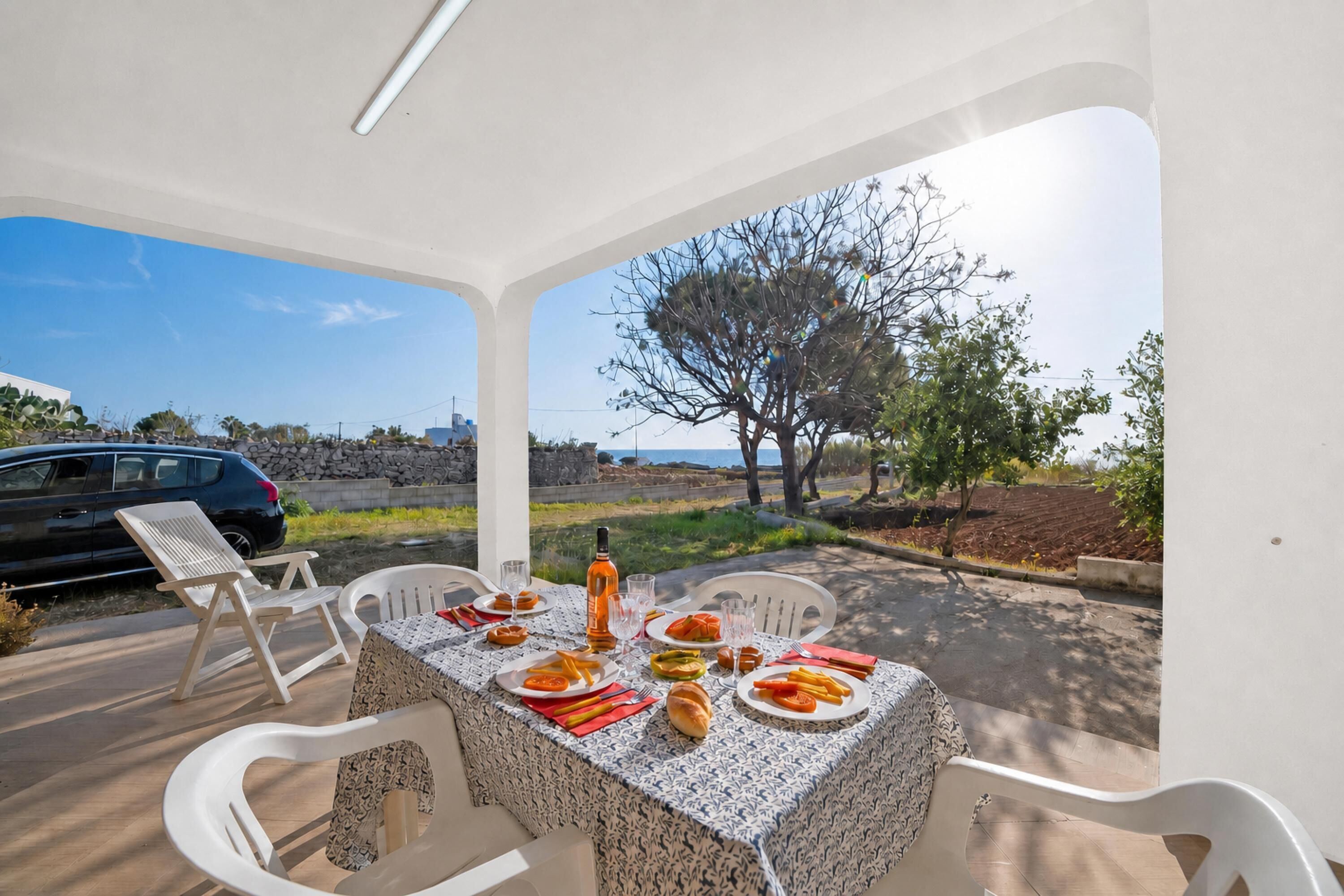 An outdoor dining area with a table set for two, chairs, and a view of the sea.