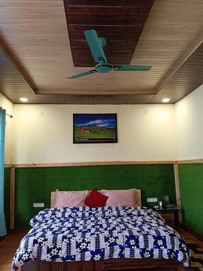 Quarto com teto de madeira, ventoinha no teto, cama com colcha floral, paredes com grama sintética verde e uma moldura com a imagem de um cavalo.