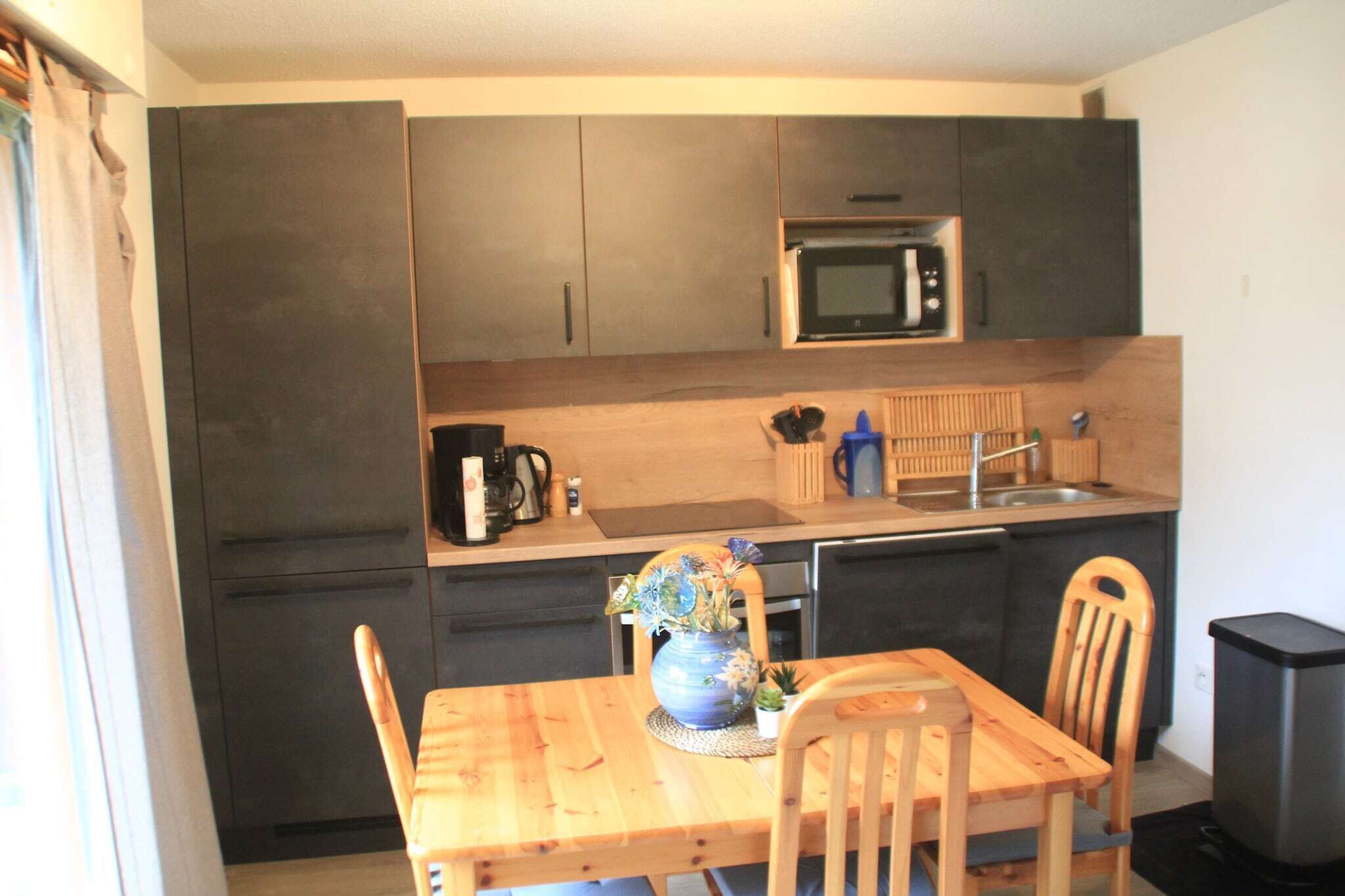 A compact kitchen with dark cabinets, a microwave, a sink, and a wooden dining table with chairs.
