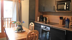Une cuisine compacte avec des meubles de couleur sombre, un four à micro-ondes, une machine à café et un coin repas comprenant une table et des chaises en bois.