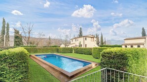 A rectangular swimming pool surrounded by well-manicured hedges, with a clear blue sky and distant mountains in the background. - Family Tuscany Villa with private pool (Civitella in Val di Chiana)