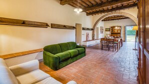 A spacious living area with a green sofa, a white sofa, and a dining table with chairs. The room features a tiled floor, wooden beams on the ceiling, and an arched doorway leading to another room. - Family Tuscany Villa with private pool (Civitella in Val di Chiana)