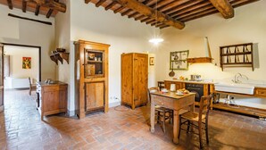 A rustic kitchen with wooden cabinets, a dining table, and a tiled floor. - Family Tuscany Villa with private pool (Civitella in Val di Chiana)