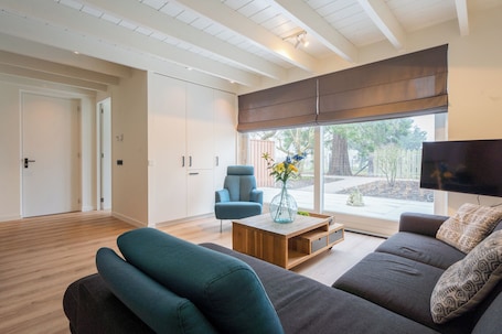 A modern living room with a sofa, armchair, and coffee table. There is a large window with a view of the outdoors.