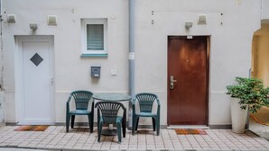 A small outdoor seating area with a table and two chairs, a white door with a diamond-shaped window, and a brown door with a sign. - Red Vibe Studio Central 2 (Zagreb)