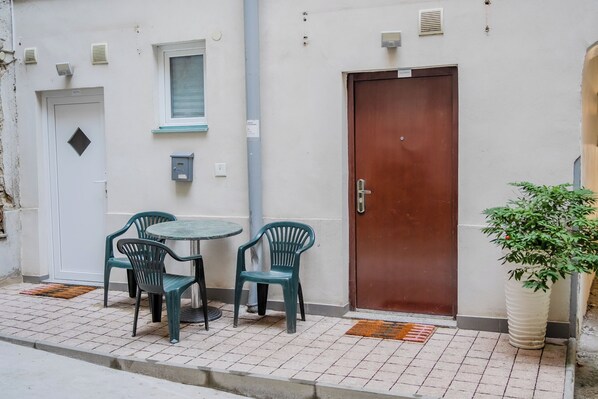 Un pequeño espacio al aire libre con una mesa y cuatro sillas, una puerta marrón y una planta en maceta.