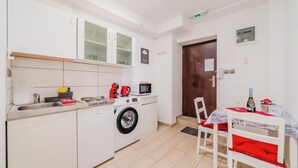 A compact kitchen with a washing machine, microwave, and a small dining area with a table and chairs. - Red Vibe Studio Central 2 (Zagreb)