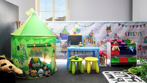 Une salle de jeux pour enfants avec une tente verte, une table bleue et une bibliothèque remplie de jouets.