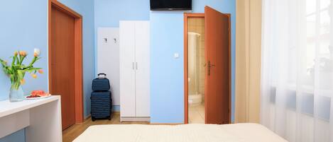A hotel room with a bed, a desk with a vase of flowers, a suitcase, a television, and a bathroom visible through an open door.