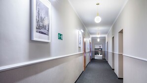 Un couloir aux murs ornés de tableaux encadrés, un panneau de signalisation verte indiquant la sortie et un sol recouvert de moquette.