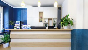 Un comptoir d’accueil avec un revêtement en bois clair, des étagères blanches et des plantes en pot.