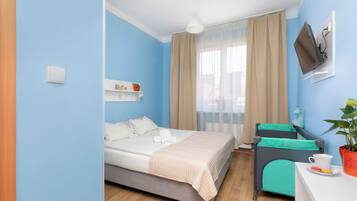 A hotel room with a bed, a desk, a chair, a TV, and a window with curtains.