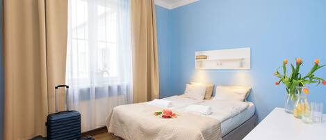 Una habitación de hotel con cama, escritorio, maleta y un florero con flores.