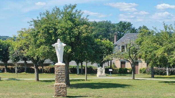 Un cementerio con estatuas blancas, un pilar de piedra y una casa al fondo.