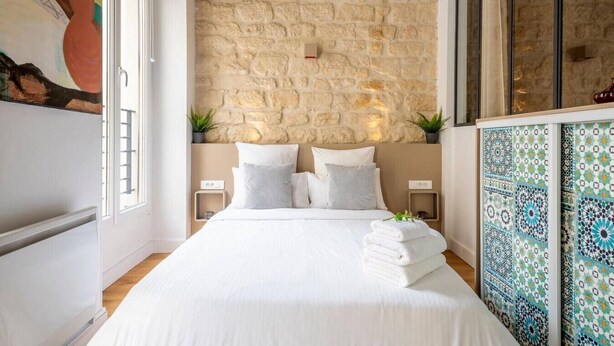 A bedroom with a stone wall, a bed with white linens, two bedside tables, and a patterned cabinet. - #République#Paris2#Chatelêt#2bedrooms (Paris)