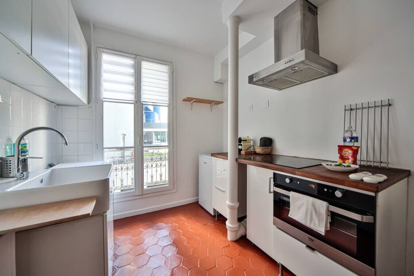 Una cocina con armarios blancos, estufa, pileta y ventana con persianas.