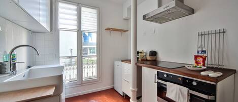 Una cocina con armarios blancos, estufa, pileta y ventana con persianas.