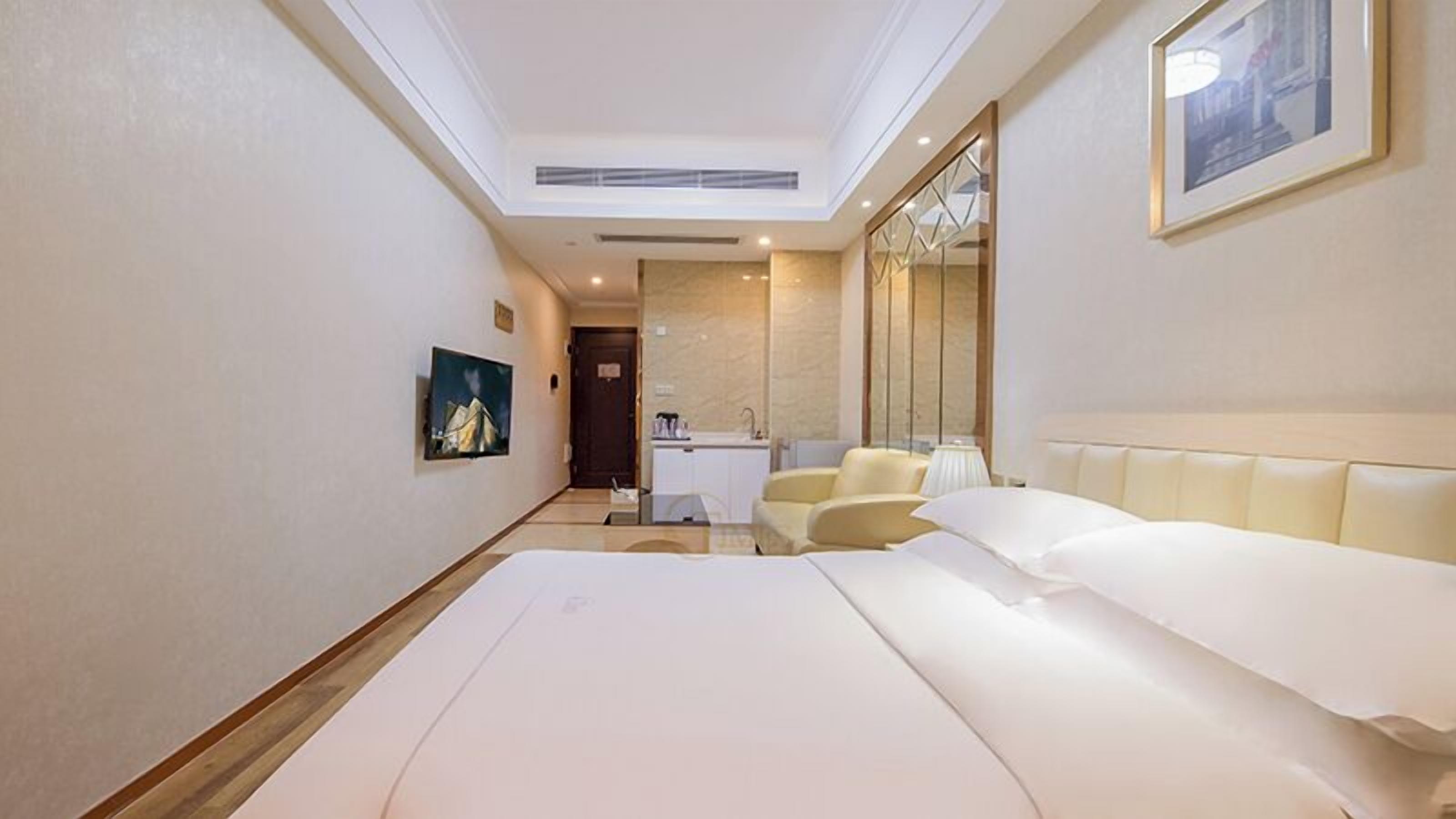 A hotel room with a large bed, a sitting area with chairs, a small desk, a mirror, and a television on the wall.