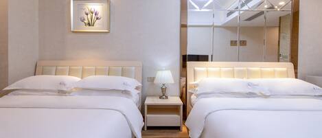 A hotel room with two beds, a bedside table with a lamp, a framed picture on the wall, and a large mirror.