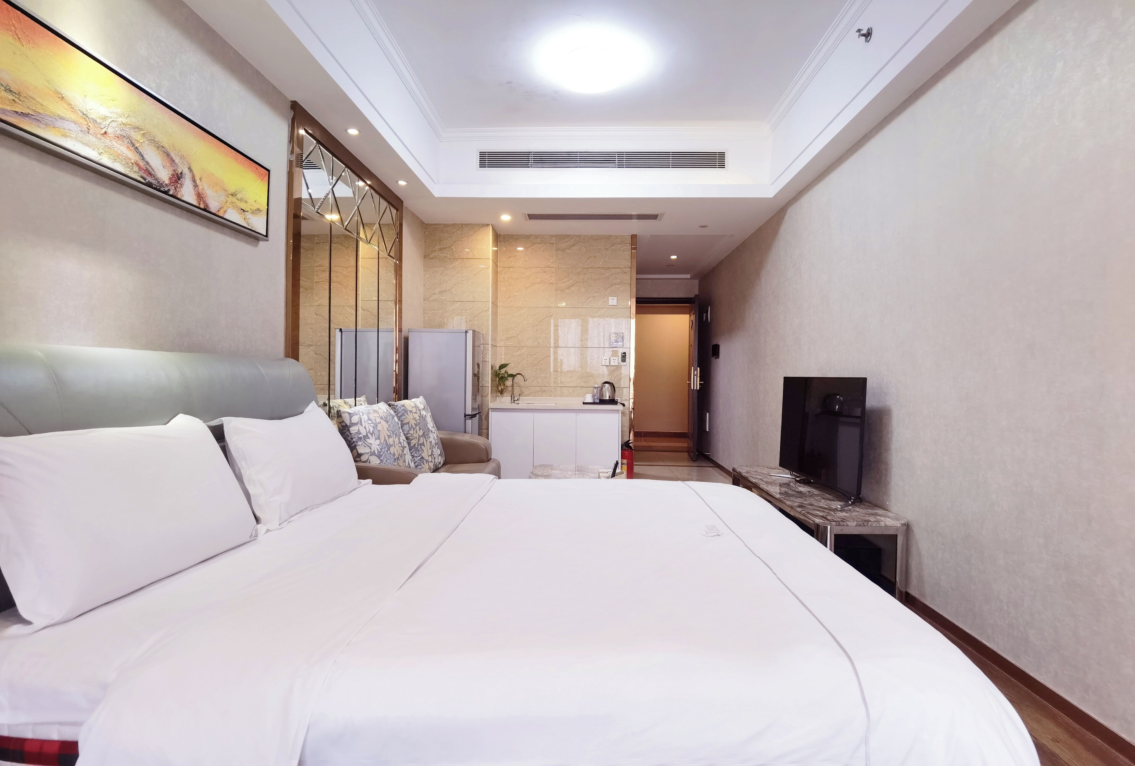 A hotel room with a large bed, a television, a small table, and a kitchenette area.