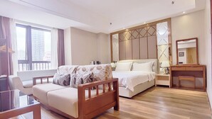 Una habitación de hotel moderna con piso de madera, un sofá, una cama con cabecera, un escritorio y un ventanal con cortinas.