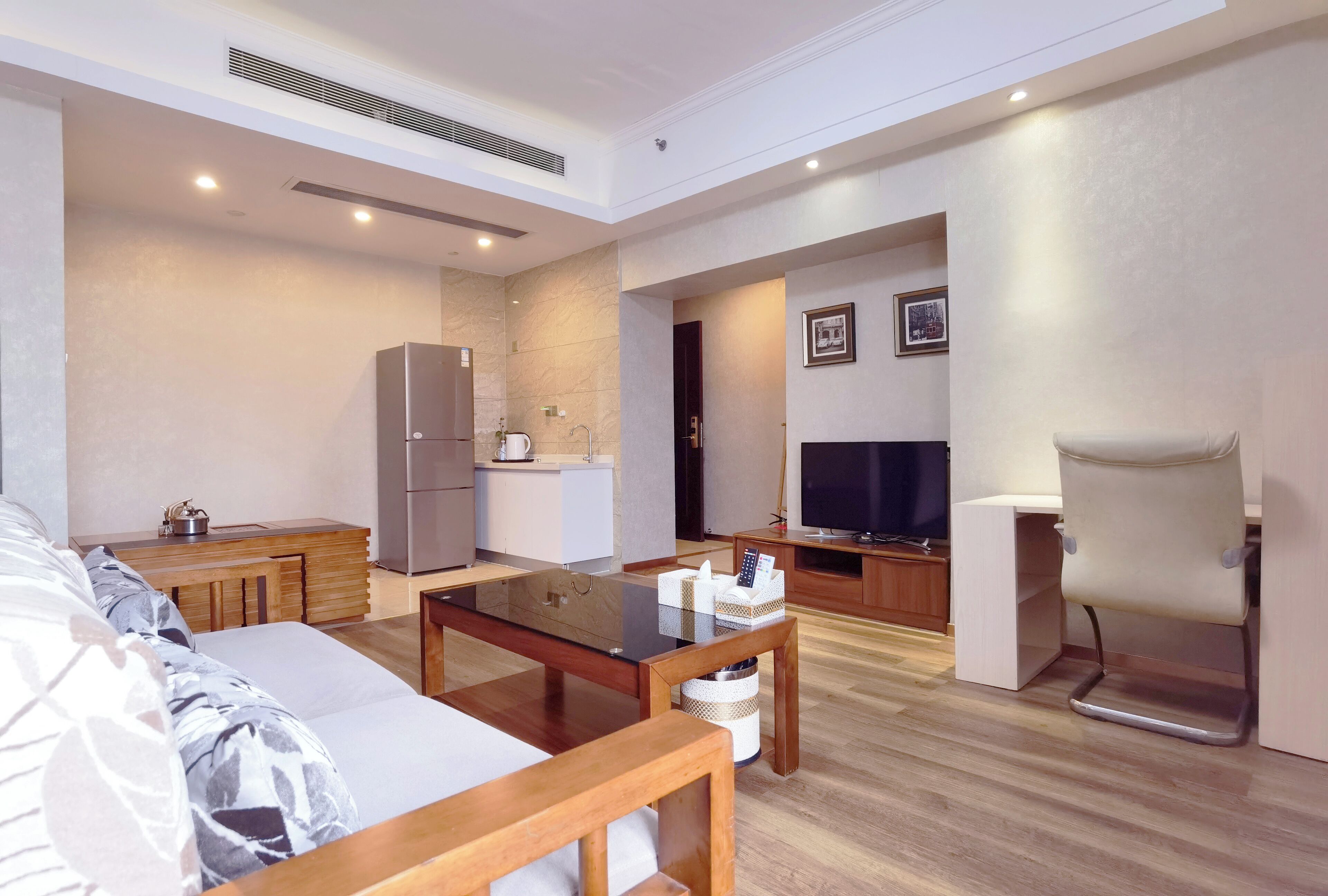 A modern living room with a sofa, a coffee table, a TV, and a kitchen area with a refrigerator and microwave.
