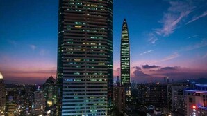 Un paisaje urbano al anochecer con rascacielos, incluyendo un rascacielos destacado con un techo puntiagudo y otro con fachada curva.