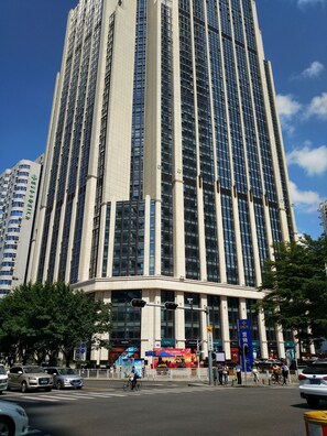 Un edificio alto y moderno con una fachada de ventanas en forma de cuadrícula y una entrada destacada.