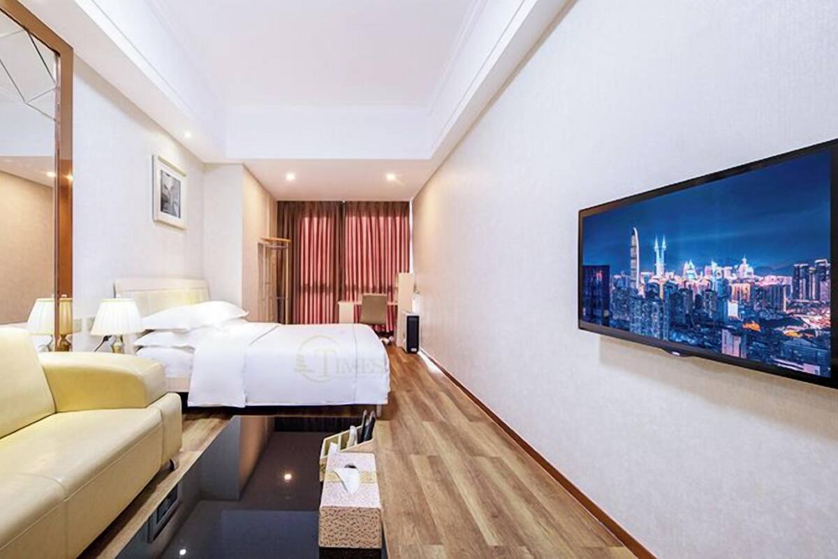 Habitación de hotel con cama, sofá, televisión y vista panorámica de la ciudad.