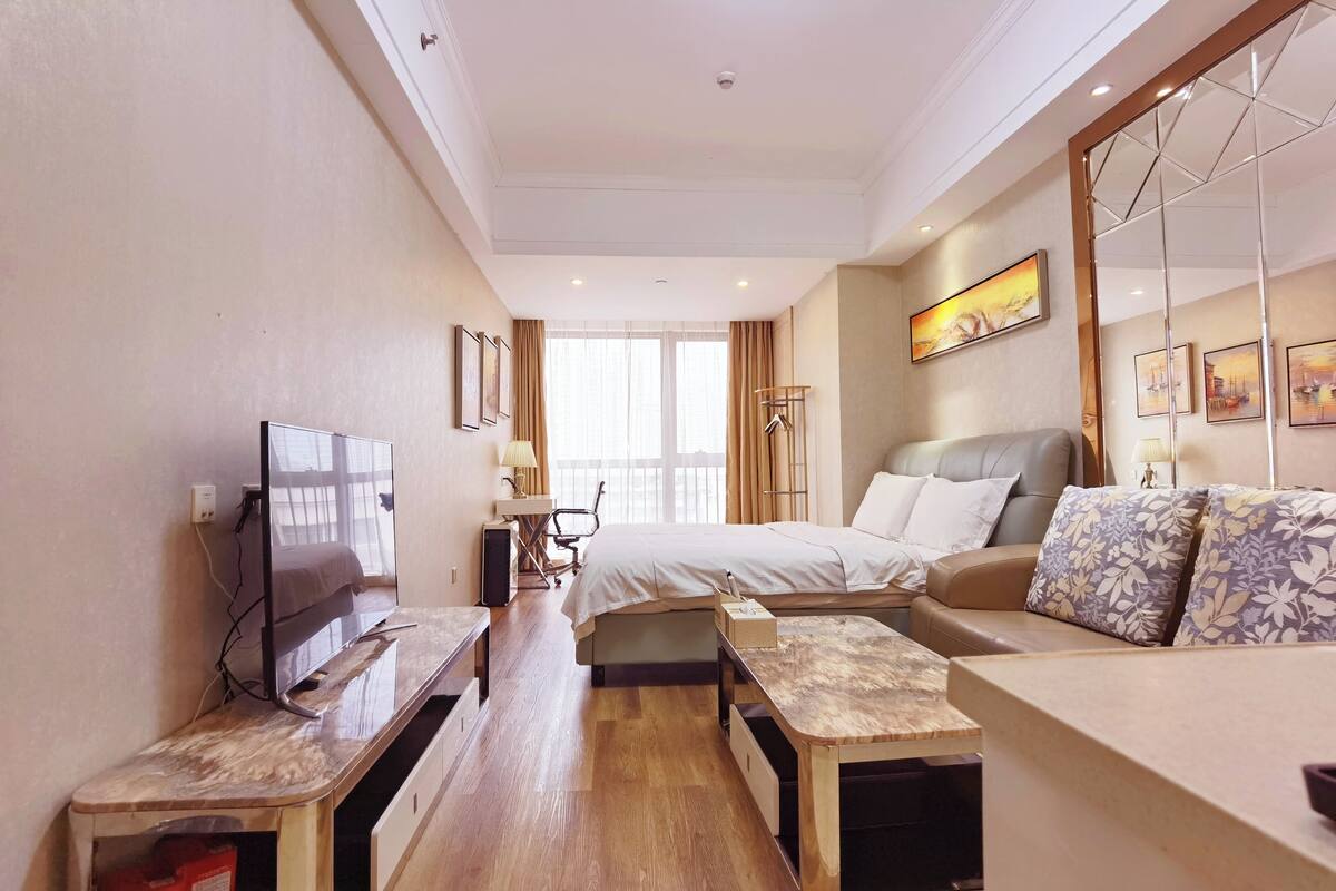 Una habitación de hotel con cama, sofá, televisión, escritorio y ventana con cortinas.