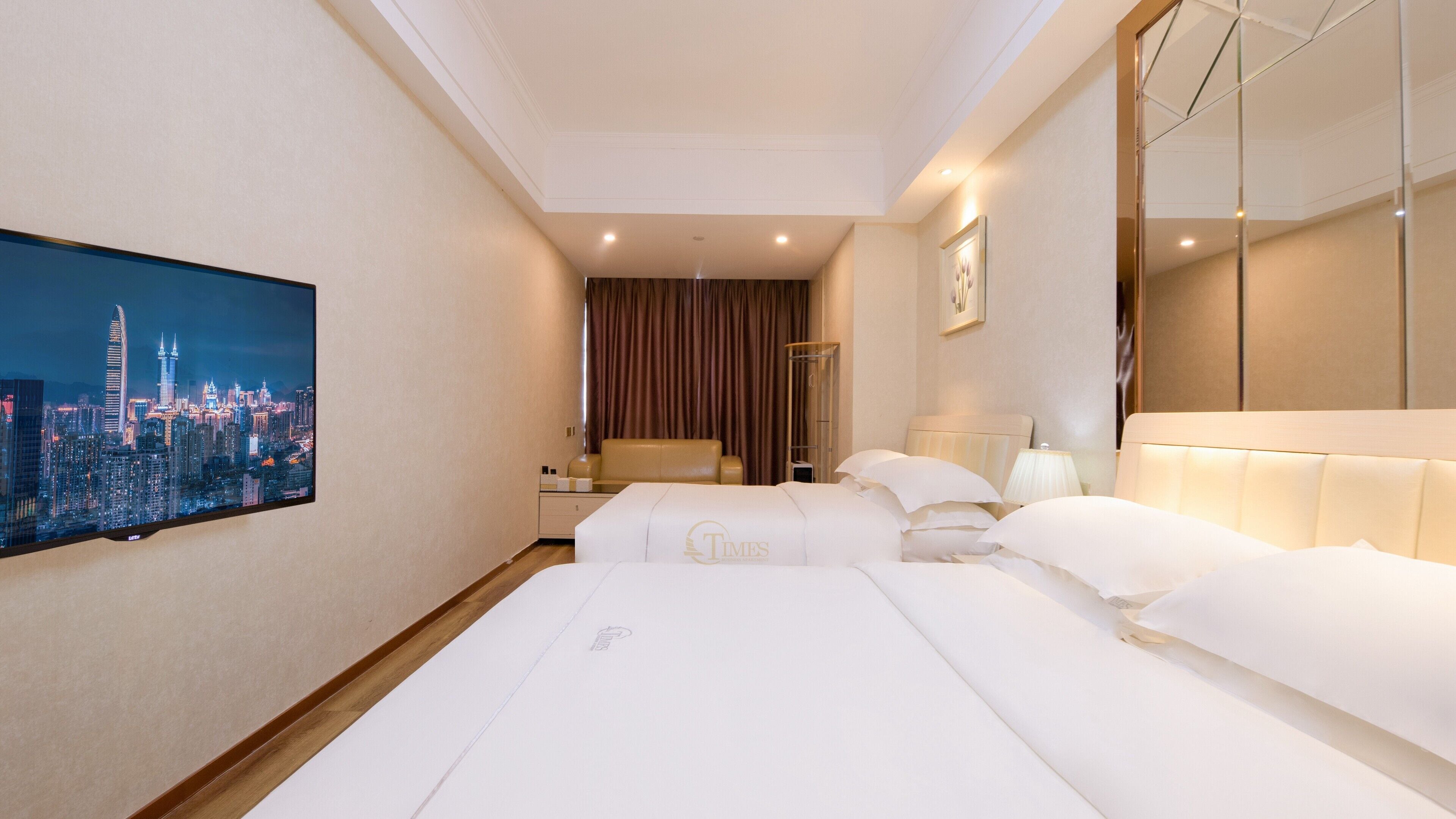 A hotel room with a cityscape view, a bed with white linens, a bedside table, a lamp, and a mirror.