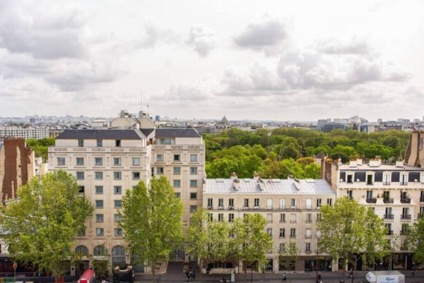 Un paisaje urbano con un edificio destacado de estilo arquitectónico clásico, rodeado de árboles y otros edificios.