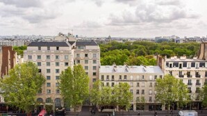 Une vue urbaine mettant en valeur un bâtiment imposant, de style architectural classique, entouré d’arbres et d’autres bâtiments.