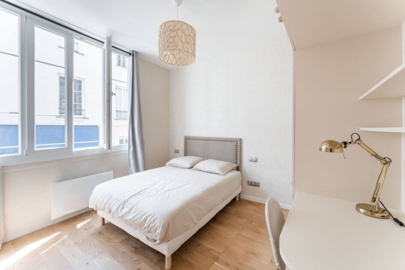 A bedroom with a bed, a desk, a lamp, and a window with curtains.