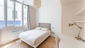 A bedroom with a bed, a desk, a lamp, and a window with curtains. - Charming home in heart of PARIS!Opera/Eurostar 4pers (Paris)