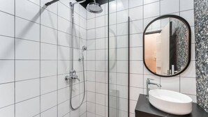 A modern bathroom with white tiled walls, a glass shower enclosure, a round mirror, and a black countertop with a white sink. - Charming home in heart of PARIS!Opera/Eurostar 4pers (Paris)