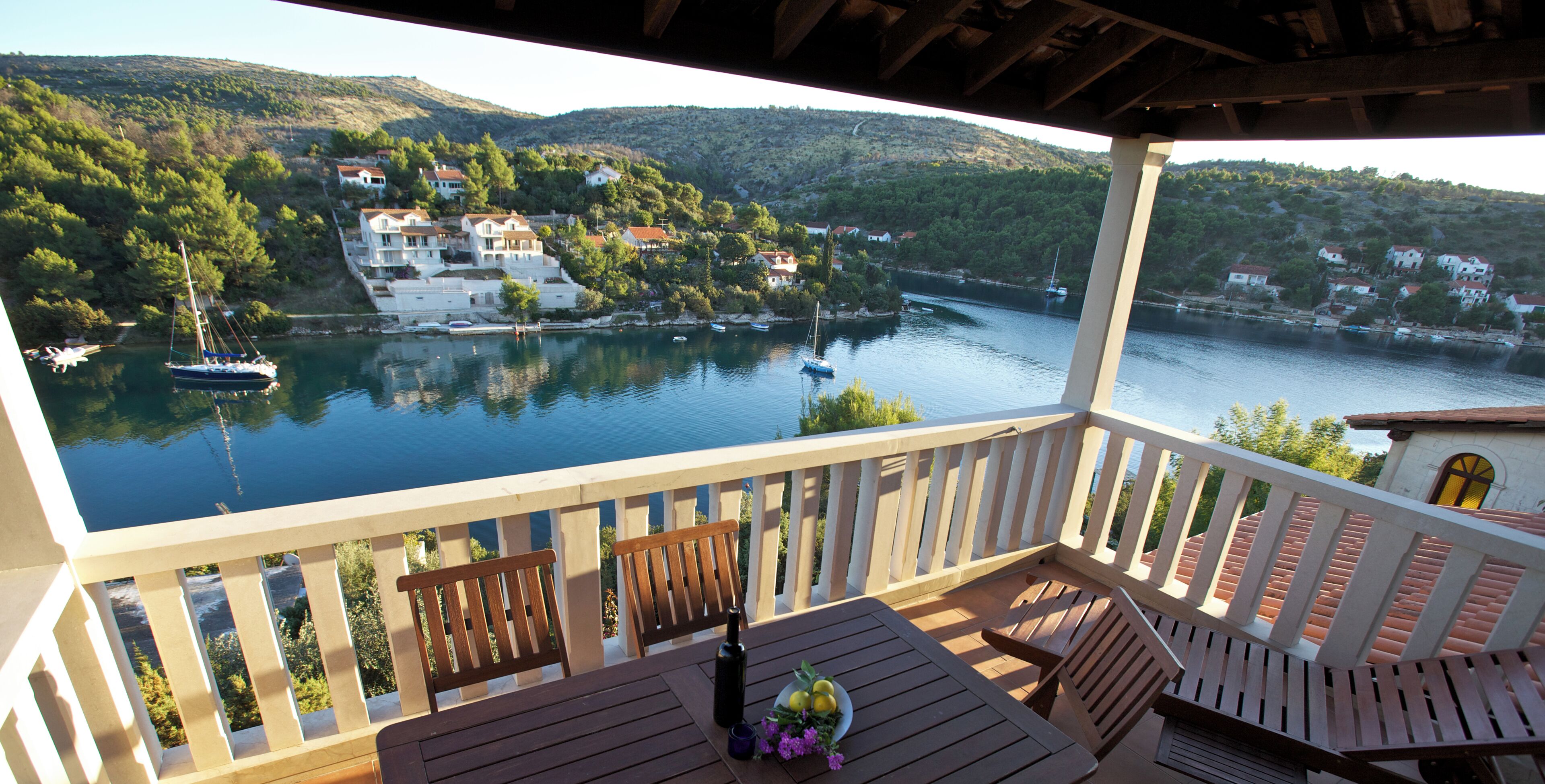 A wooden deck with a table and chairs overlooking a lake with boats and houses.