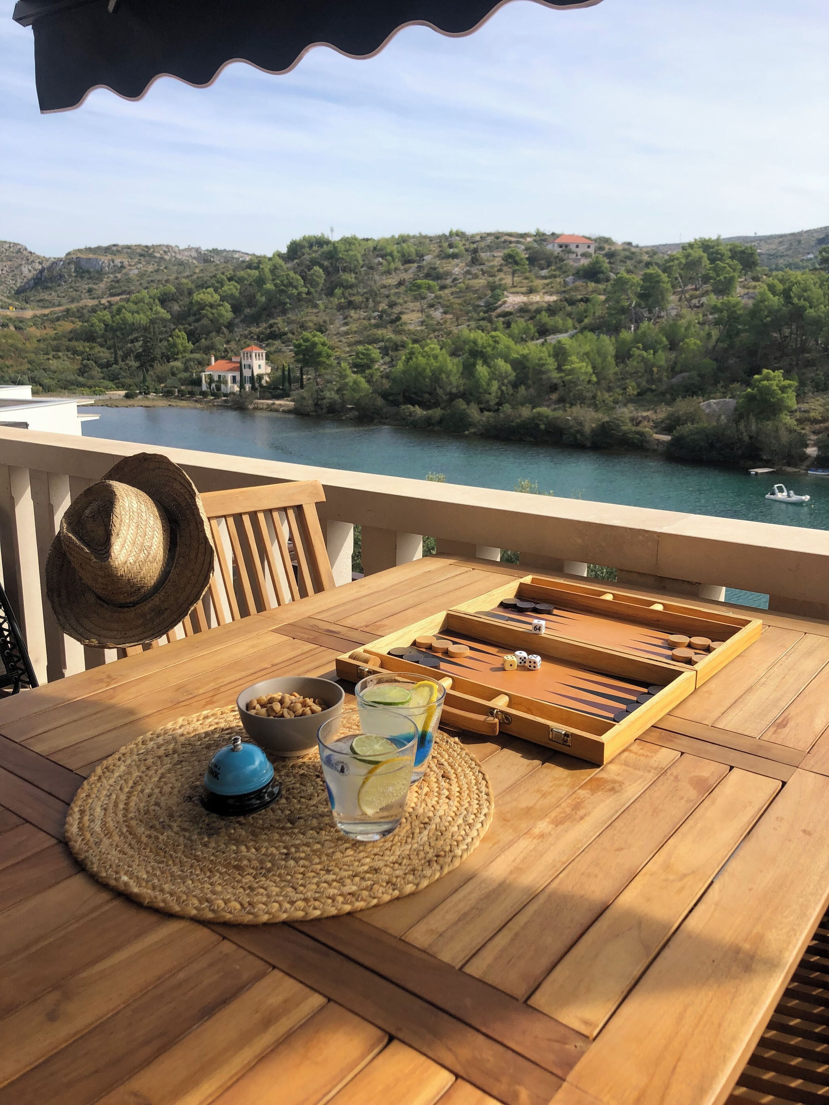 Une table en bois donnant sur un lac et des collines, un chapeau, un bol de collations et un jeu de société.