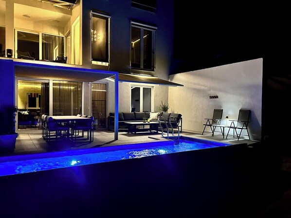 Una casa moderna con piscina, mobiliario exterior y un ventanal grande con vistas a la piscina.