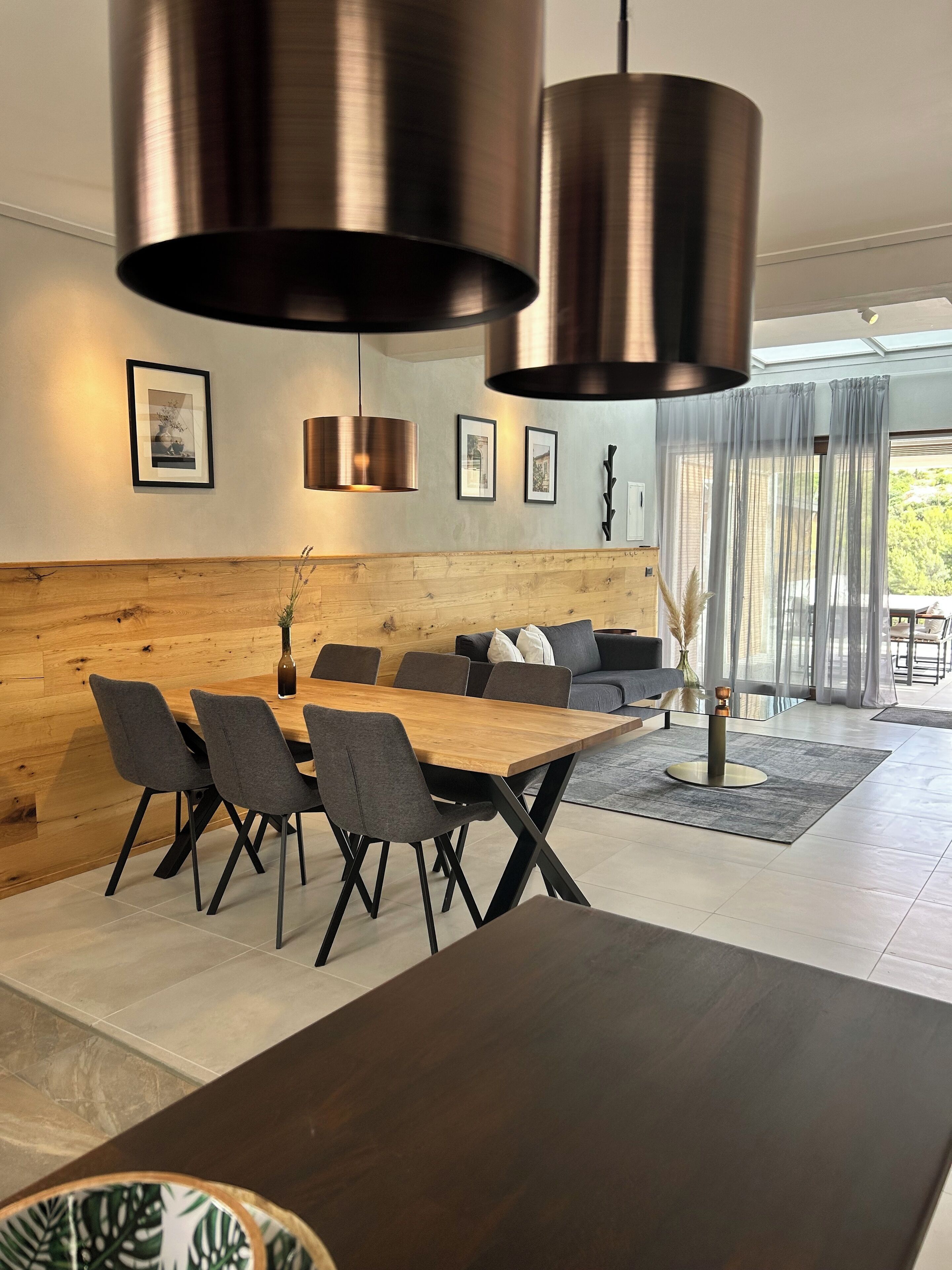 A modern dining area with a wooden table and chairs, a sofa, and a large window with curtains.