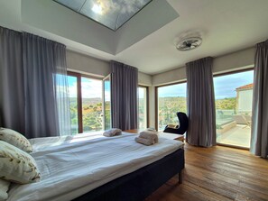 Un dormitorio con una cama grande, un ventilador de techo y vistas a una ladera a través de amplios ventanales.