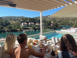 Una terraza con piscina, mesa de desayuno y vistas panorámicas de un lago y edificios.