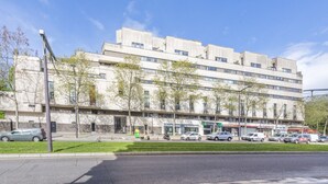 A multi-story building with a flat facade, several ground-level commercial spaces, and a parking lot with cars. - New Duplex 6Pers#Paris Expo#Porte de Versailles (Paris)