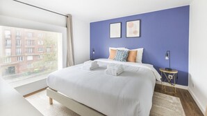 A modern hotel room with a large bed, a view of a cityscape, and a small side table with a lamp. - New Duplex 6Pers#Paris Expo#Porte de Versailles (Paris)
